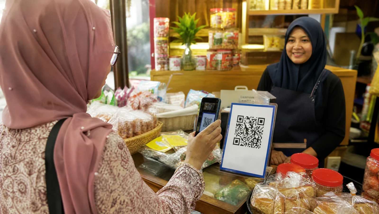 A customer scanning a DuitNow QR code with a smartphone to pay a Malaysian small business