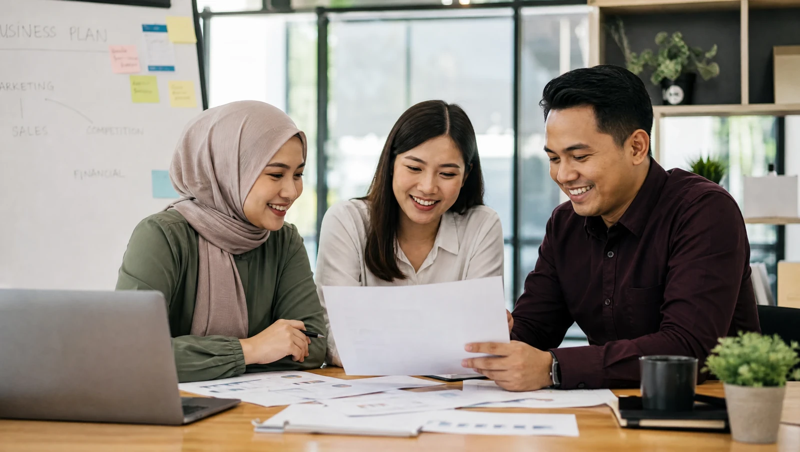 A small Malaysian business team reviewing paperwork together, looking relieved