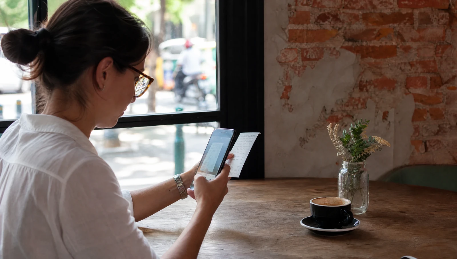 A small business owner photographing a receipt with a smartphone at a cafe table